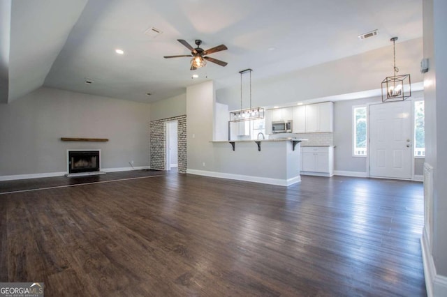 unfurnished living room featuring ceiling fan with notable chandelier, vaulted ceiling, and dark wood-type flooring