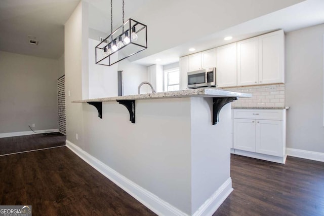 kitchen featuring a breakfast bar, dark hardwood / wood-style floors, pendant lighting, and white cabinets