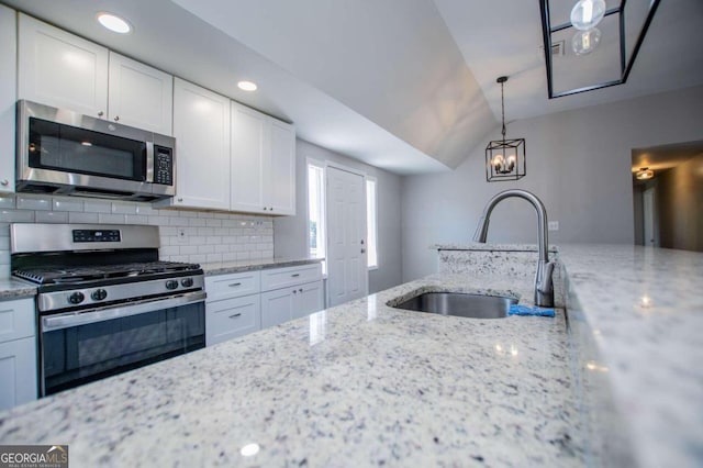 kitchen with appliances with stainless steel finishes, light stone counters, white cabinets, lofted ceiling, and sink