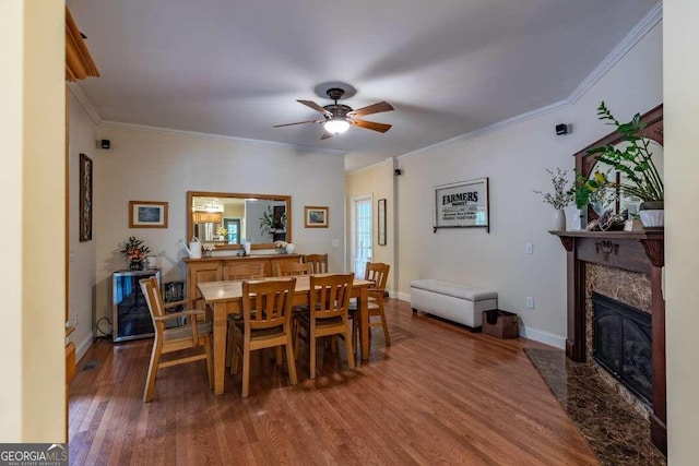 dining room featuring wood-type flooring, crown molding, a premium fireplace, and ceiling fan