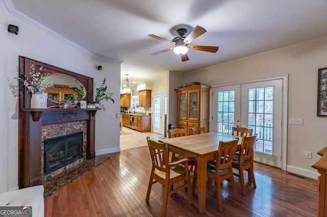 dining room with ceiling fan, french doors, hardwood / wood-style flooring, a premium fireplace, and crown molding