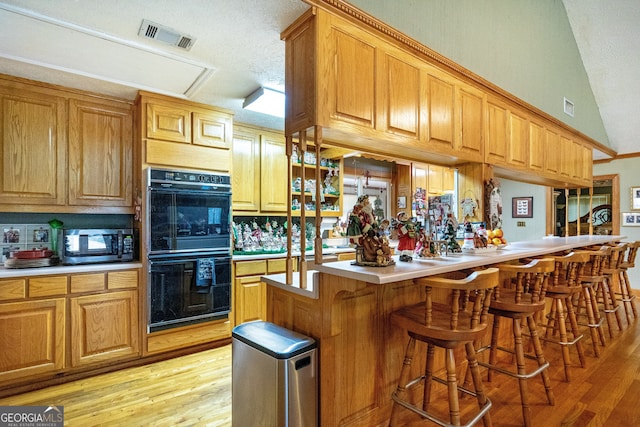 kitchen featuring double oven, light wood-type flooring, vaulted ceiling, and a breakfast bar