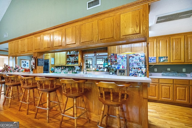 kitchen featuring kitchen peninsula, a breakfast bar area, light wood-type flooring, fridge with ice dispenser, and sink