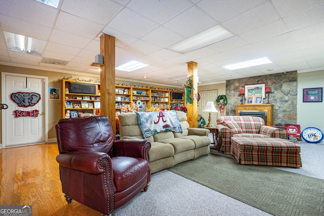 living room with a paneled ceiling, a stone fireplace, and hardwood / wood-style flooring