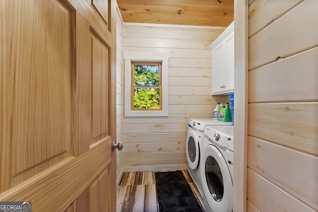 laundry room featuring cabinets, wood-type flooring, wood walls, and washing machine and clothes dryer