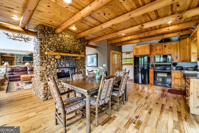 dining space with light wood-type flooring, wood ceiling, a stone fireplace, and beamed ceiling