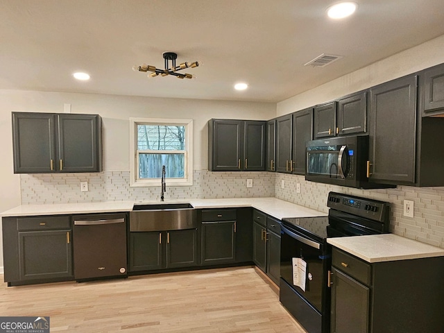 kitchen featuring light wood finished floors, light countertops, visible vents, a sink, and black appliances