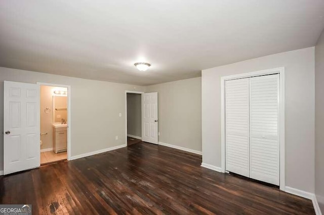 unfurnished bedroom featuring ensuite bathroom, a closet, and dark hardwood / wood-style flooring