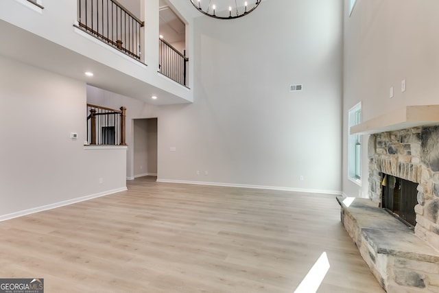 unfurnished living room featuring light hardwood / wood-style floors, a fireplace, a high ceiling, and a chandelier