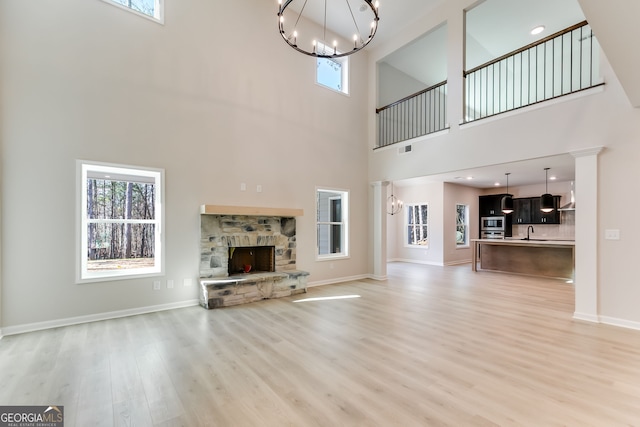 unfurnished living room featuring a towering ceiling, light hardwood / wood-style floors, a stone fireplace, and plenty of natural light