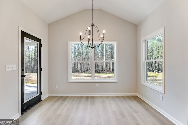 unfurnished dining area with light hardwood / wood-style flooring, a healthy amount of sunlight, lofted ceiling, and an inviting chandelier