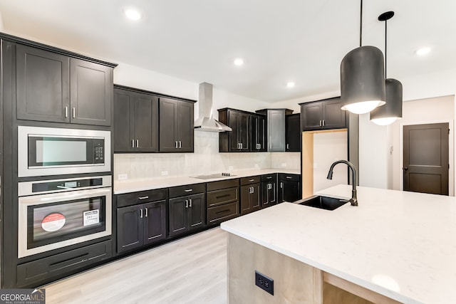 kitchen with pendant lighting, wall chimney range hood, sink, light hardwood / wood-style flooring, and appliances with stainless steel finishes