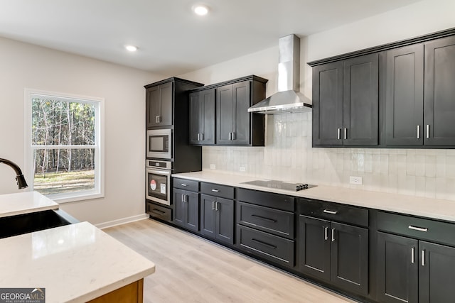 kitchen with decorative backsplash, light wood-type flooring, wall chimney exhaust hood, stainless steel appliances, and sink