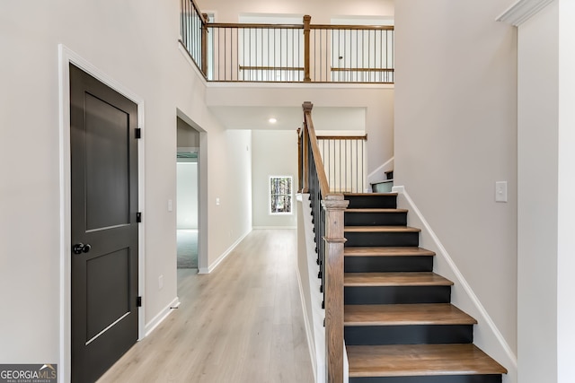 stairway with wood-type flooring and a towering ceiling