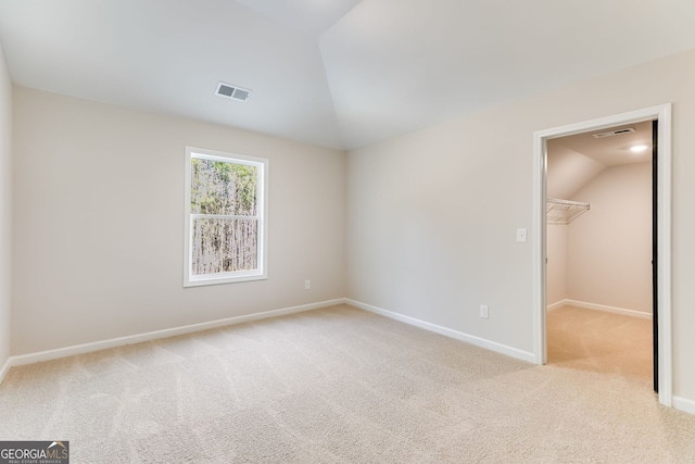 unfurnished bedroom featuring a spacious closet, a closet, light colored carpet, and lofted ceiling