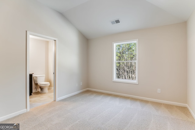 unfurnished bedroom with connected bathroom, light carpet, and lofted ceiling