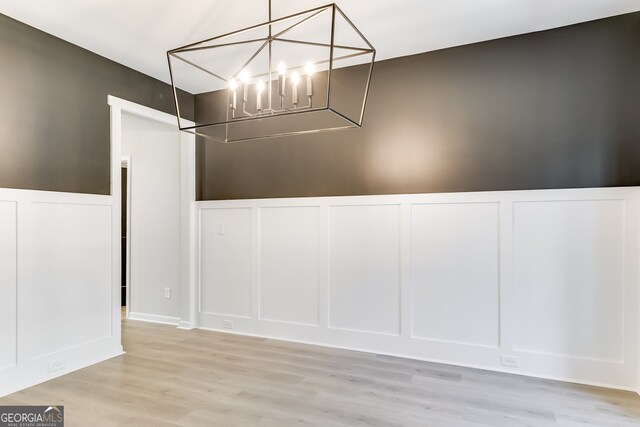 unfurnished dining area featuring an inviting chandelier and light hardwood / wood-style flooring