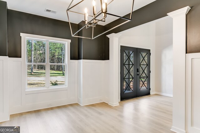 entryway with ornate columns, a notable chandelier, and light wood-type flooring