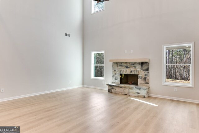 unfurnished living room with a fireplace, a high ceiling, and light wood-type flooring