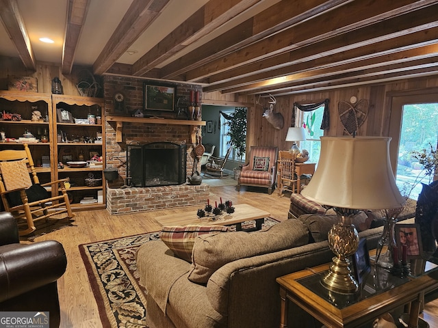 living room with beam ceiling, wooden walls, hardwood / wood-style floors, and a brick fireplace