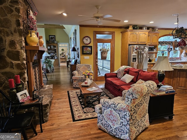 living room with crown molding, a stone fireplace, hardwood / wood-style floors, and ceiling fan