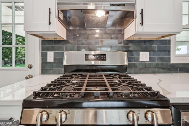 kitchen with light stone counters, backsplash, white cabinetry, ventilation hood, and gas stove