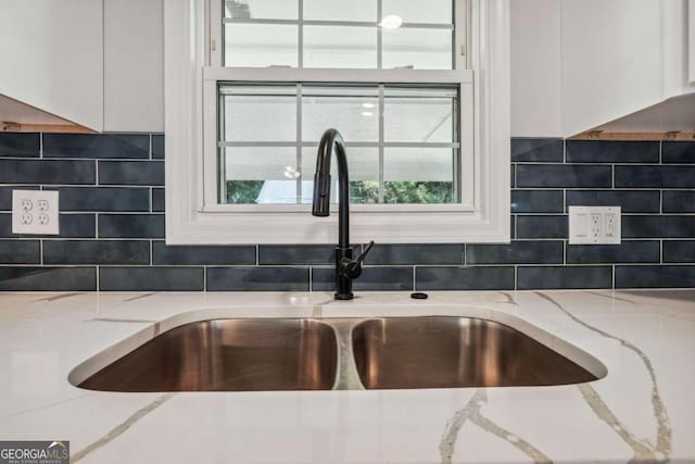 interior details featuring backsplash, light stone counters, and sink