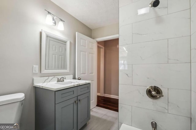 bathroom featuring a textured ceiling, hardwood / wood-style floors, tiled shower, vanity, and toilet