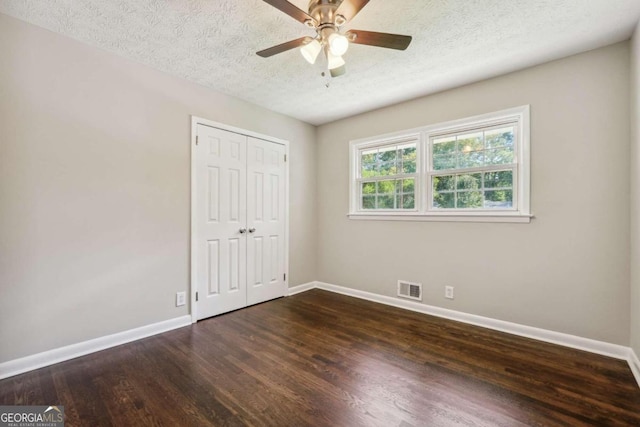 unfurnished bedroom with ceiling fan, a textured ceiling, a closet, and dark hardwood / wood-style flooring