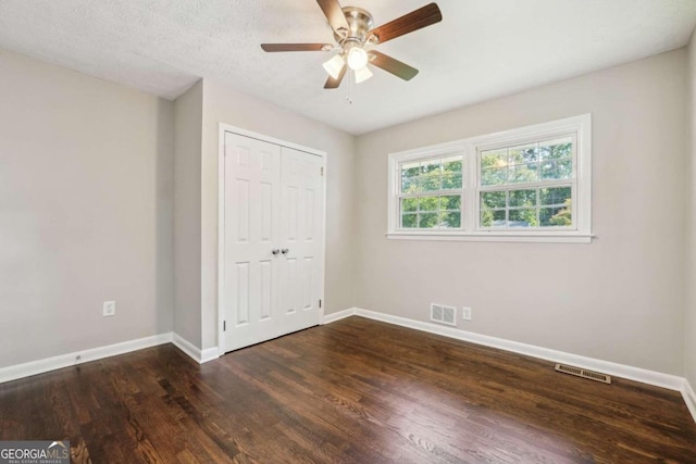 unfurnished bedroom with ceiling fan, a textured ceiling, a closet, and dark wood-type flooring