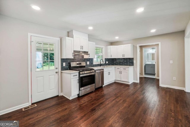 kitchen with appliances with stainless steel finishes, white cabinets, backsplash, dark hardwood / wood-style flooring, and sink