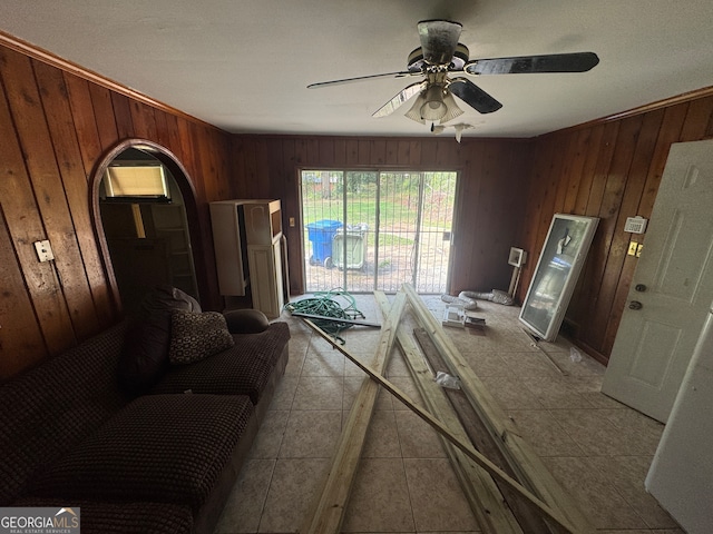 living room with wood walls, ceiling fan, and light tile patterned floors