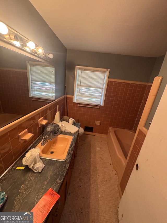 bathroom featuring tile walls, a bathing tub, vanity, toilet, and tile patterned floors