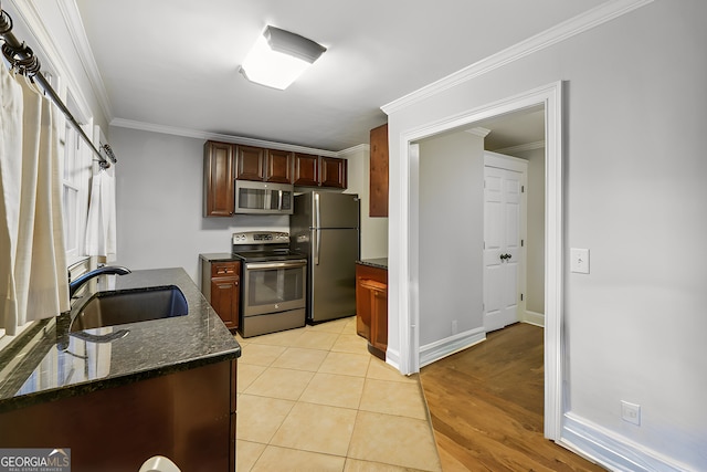 kitchen featuring light wood-type flooring, stainless steel appliances, dark stone countertops, sink, and ornamental molding