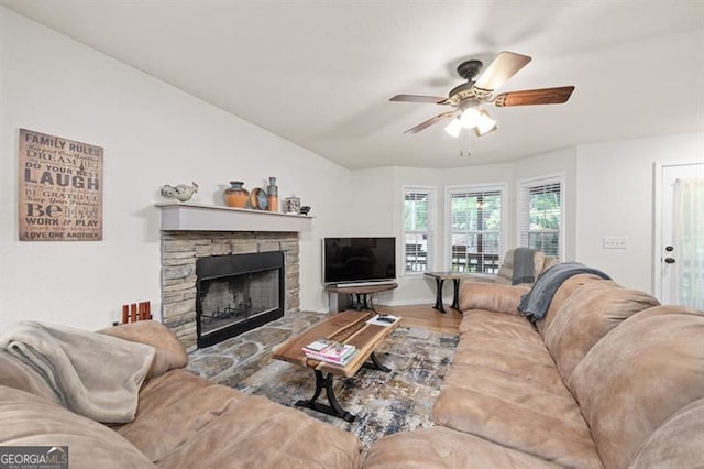 living room featuring ceiling fan, a stone fireplace, and wood-type flooring