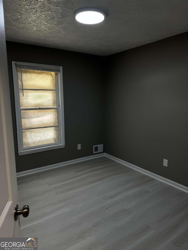 spare room with a textured ceiling and light hardwood / wood-style flooring