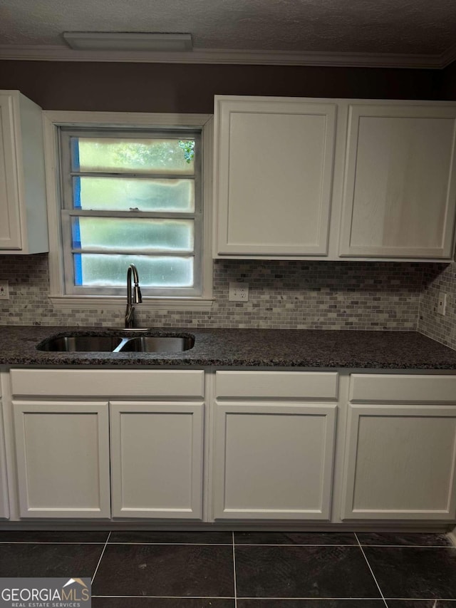 kitchen with backsplash, dark stone countertops, sink, and white cabinets