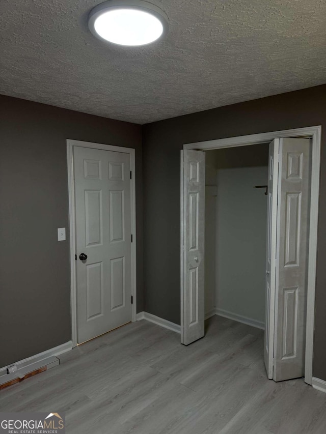 unfurnished bedroom with a textured ceiling, light hardwood / wood-style floors, and a closet