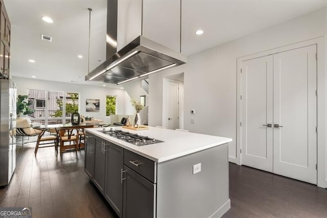 kitchen featuring wall chimney exhaust hood, gray cabinetry, stainless steel appliances, dark wood-type flooring, and a kitchen island