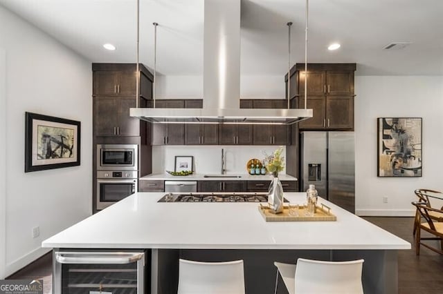 kitchen with stainless steel appliances, wine cooler, a center island with sink, and exhaust hood