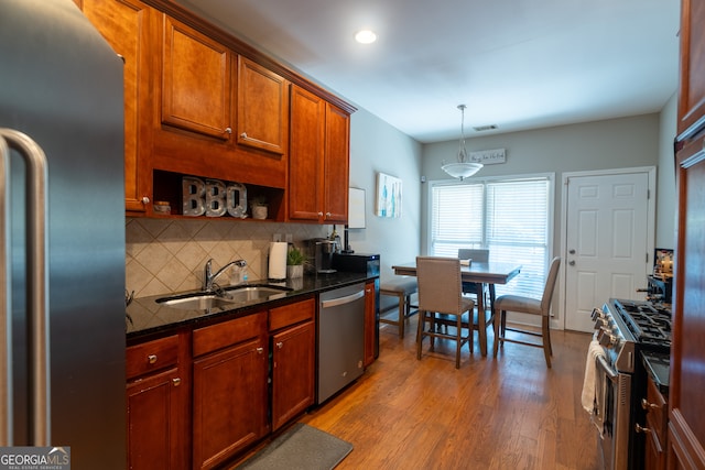 kitchen featuring hanging light fixtures, sink, light hardwood / wood-style flooring, appliances with stainless steel finishes, and dark stone counters