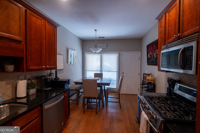 kitchen with light hardwood / wood-style floors, decorative backsplash, dark stone countertops, stainless steel appliances, and hanging light fixtures