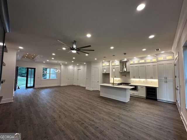 kitchen with ceiling fan, white cabinets, beverage cooler, a center island with sink, and dark wood-type flooring