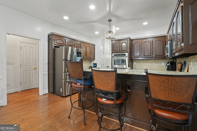 kitchen featuring dark brown cabinetry, ornamental molding, stainless steel appliances, a breakfast bar, and light wood-type flooring