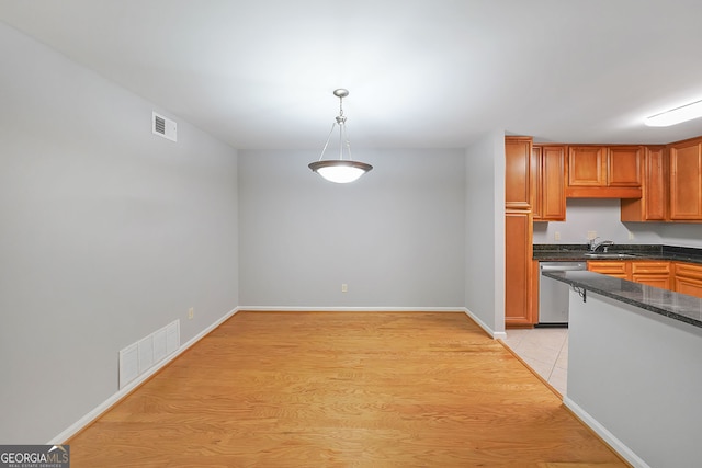 kitchen with dark stone countertops, dishwasher, light hardwood / wood-style flooring, and decorative light fixtures