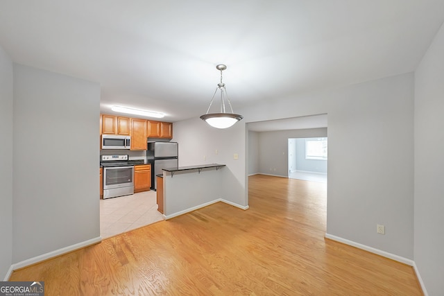 kitchen with light wood-type flooring, kitchen peninsula, appliances with stainless steel finishes, and hanging light fixtures