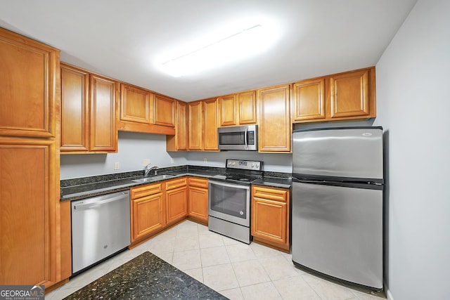 kitchen featuring dark stone countertops, sink, light tile patterned floors, and stainless steel appliances