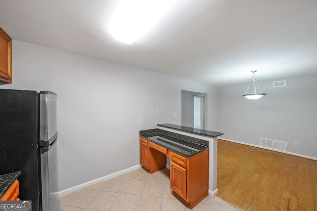 kitchen featuring light hardwood / wood-style floors, kitchen peninsula, hanging light fixtures, stainless steel refrigerator, and dark stone countertops