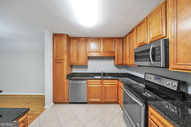 kitchen featuring stainless steel appliances, dark stone countertops, light hardwood / wood-style floors, and sink