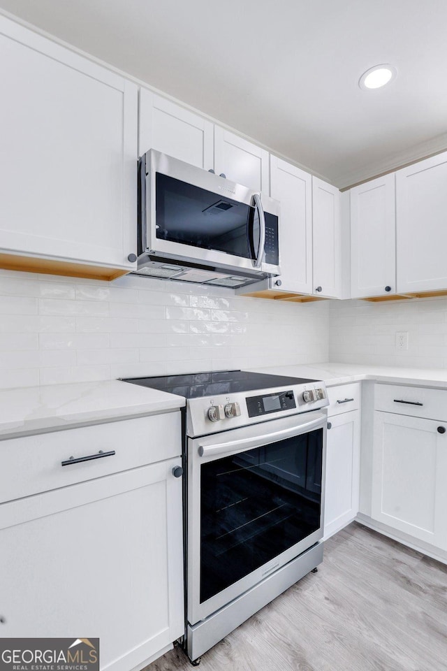 kitchen with light hardwood / wood-style floors, white cabinetry, range, and backsplash